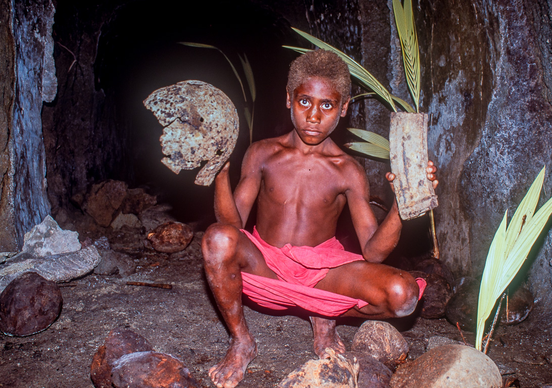 Ce jeune papou nous présente un casque et le chargeur d'un fusil mitrailleur q'il a découverts dans cette grotte.