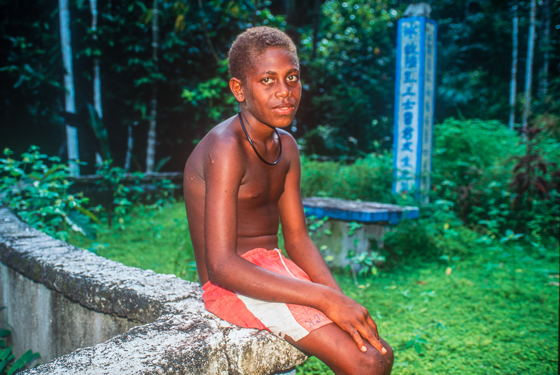 Un jeune papou, devant  un mémorial et ses idéogrammes japonais.