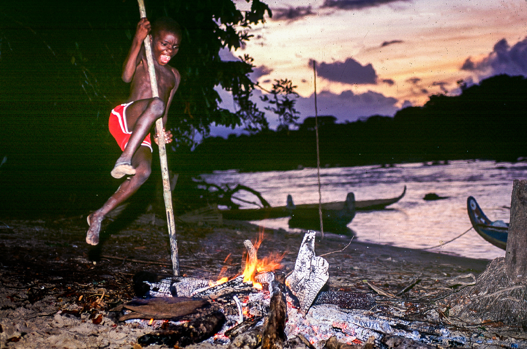 Un enfant s'amuse à sauter au dessus du feu de camp le long du fleuve Maroni.